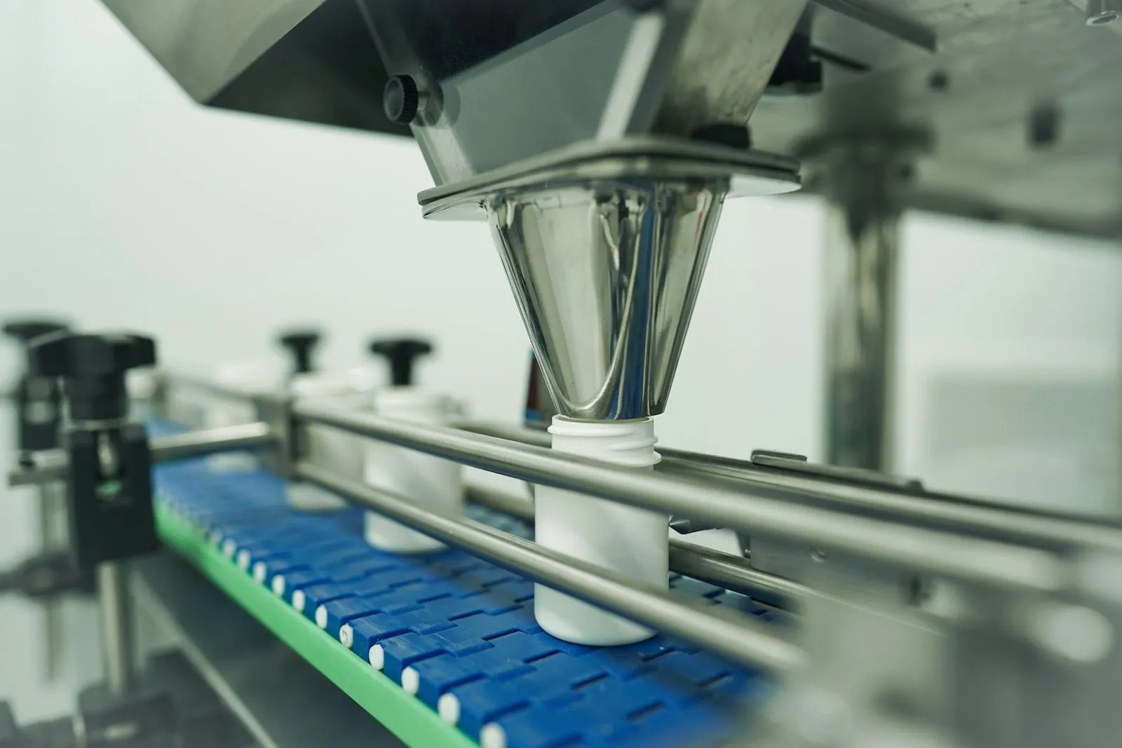 White bottles on a CPG filling line under a stainless hopper